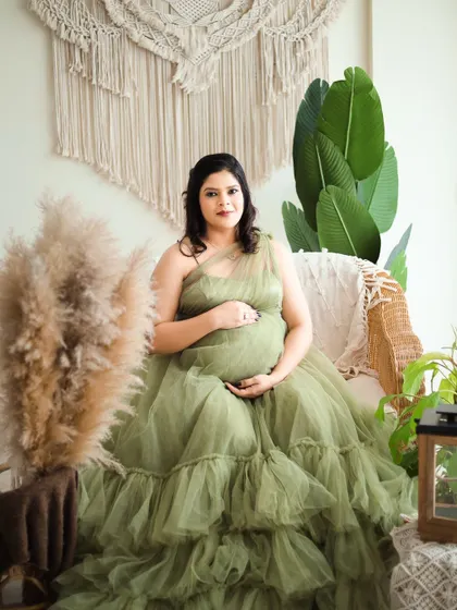 A serene portrait in our boho-themed studio. The mom-to-be is wearing a beautiful olive green gown that complements the natural decor.