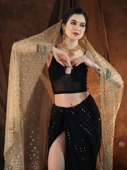 A beautiful portrait capturing the elegance of an Indo-western fusion look. The model's pose and the way she holds the sheer dupatta create a sense of grace and movement.