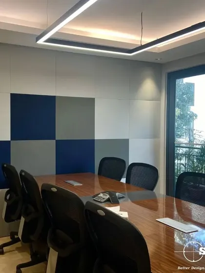 A clean and modern conference room with a large wooden table and ergonomic chairs. The wall features acoustic paneling in a checkerboard pattern to improve sound quality during important meetings.