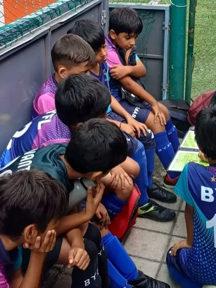 A coach giving tactical advice to the U9 team during a break in the match.