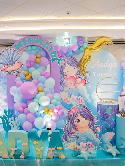 An enchanting mermaid-themed third birthday party, with a backdrop of pastel balloons and an ocean floor setting.