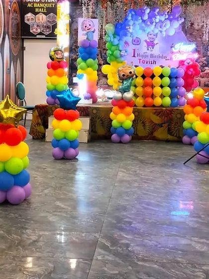 Another view of the Cocomelon party setup, showing the arrangement of rainbow balloon pillars and the main stage in a large hall.