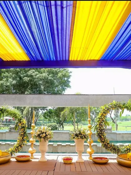 A poolside Haldi setup with circular floral wreaths and traditional brass urlis, blending modern and traditional elements.