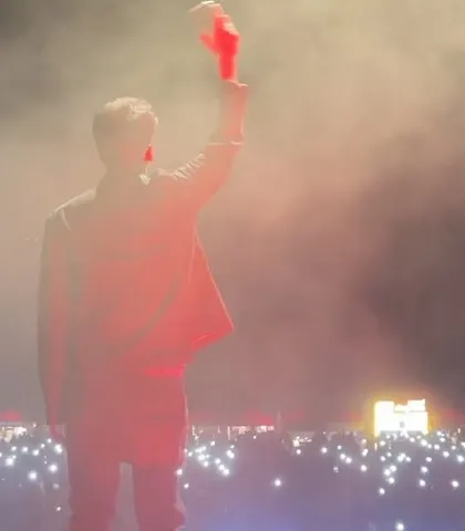Waving to the crowd, surrounded by smoke and lights.