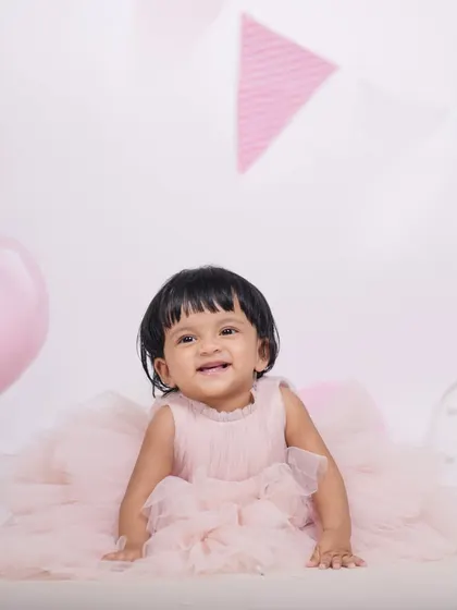Capturing the happy expressions of a baby girl during her first birthday studio photoshoot. The soft pink theme with balloons and banners creates a lovely, celebratory mood.