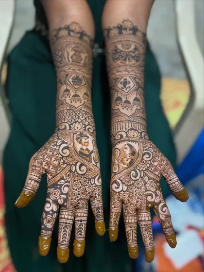 A classic bridal mehendi with bride and groom figures on the palms. The design on the arms includes traditional elements like palanquins (doli) and shehnai, symbolizing the wedding ceremony.