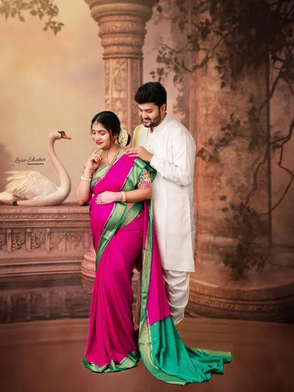 An elegant maternity portrait featuring a beautiful pink and green silk saree. The backdrop, reminiscent of ancient architecture, adds to the classic, painterly feel of the photograph.
