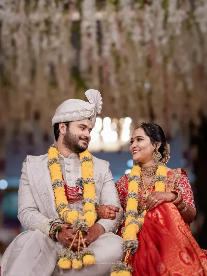 The couple shares a happy moment, seated amidst the beautiful floral decor of their wedding.