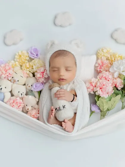 This little one is dreaming in a hammock of flowers and teddy bears, holding a tiny milk bottle. This setup combines several sweet elements for a truly unique photo.