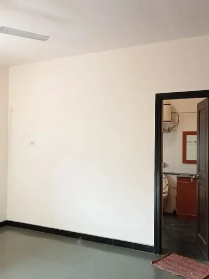 A spacious room with off-white walls, dark flooring, and a dark door frame leading to a bathroom. The clean paint job highlights the room's architectural details.