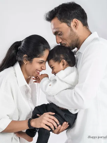 A tender moment between parents and their baby, all dressed in white. The father's gentle kiss on the baby's head speaks volumes of love.