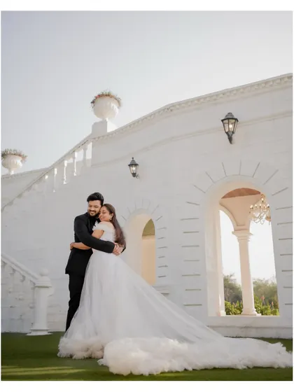 A full-length portrait of the couple against a grand white architectural backdrop. The bride's flowing gown adds a touch of drama to this pre-wedding photo.