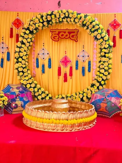 A vibrant and traditional Haldi ceremony backdrop. This setup features a stunning full circle arch made entirely of fresh yellow marigolds (genda phool) against a bright yellow curtain, with a custom 'हळद' sign in Hindi at the center.