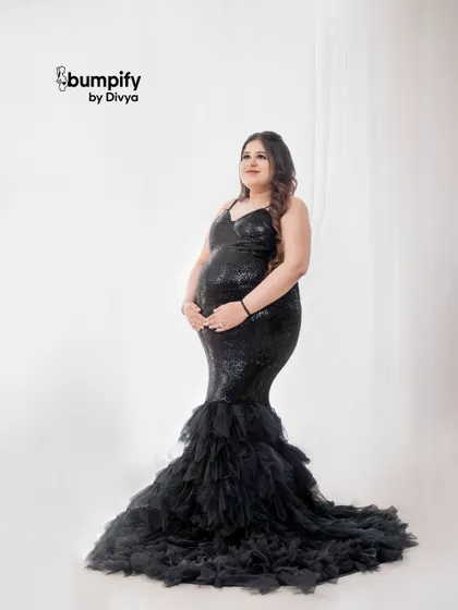 A full-length solo portrait showcasing the stunning black sequin gown. The simple white background makes the dress and the beautiful baby bump the true stars of the photo.