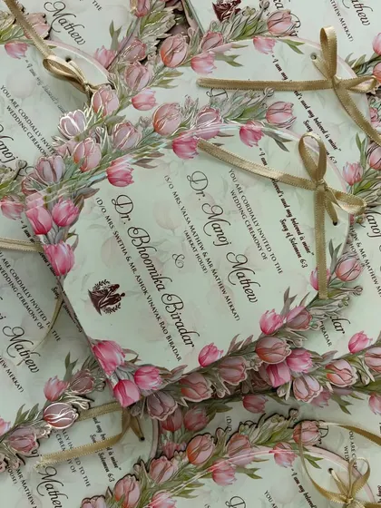A beautiful pile of my pastel lotus-themed wedding cards, tied with golden ribbons. The die-cut shape and floral border make them truly special.