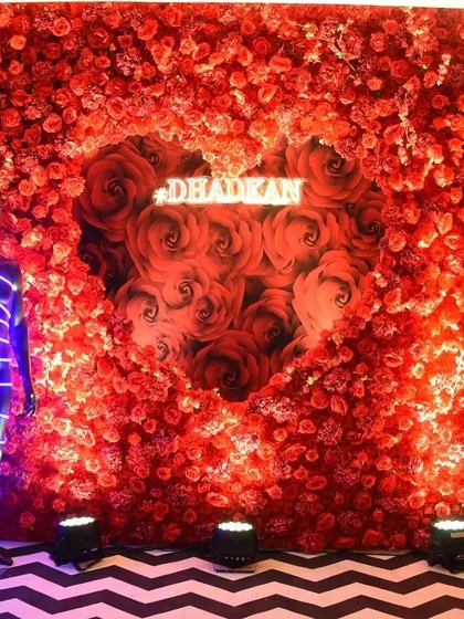 A bold and romantic photo booth. A wall of red roses with a heart-shaped cutout reveals a custom neon sign, creating a passionate and glamorous backdrop for photos.