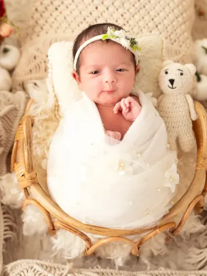 A lovely example of a boho-themed newborn shoot. This baby girl is wrapped in a simple white cloth, resting in a rattan basket surrounded by pampas grass and soft, textured fabrics.
