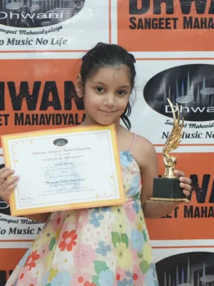 A young girl proudly holds her certificate and trophy.