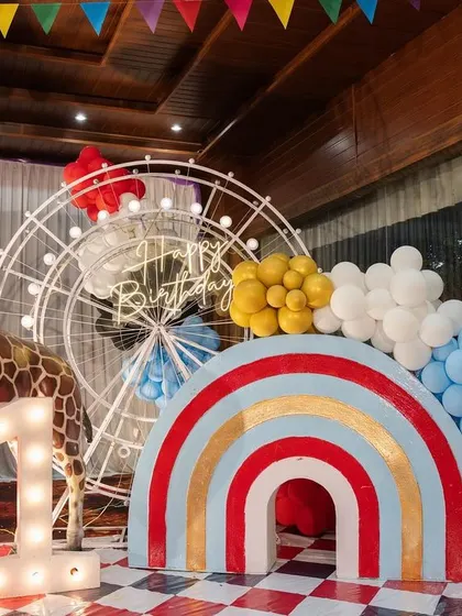 A fun photo corner at Dhiren's carnival party, with a large giraffe prop, a rainbow arch, and a light-up number '1'.