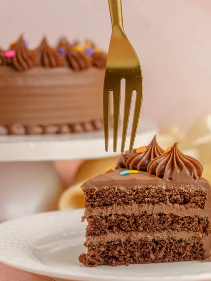 A perfect slice of the Milk Chocolate Birthday Cake, showing the rich layers of sponge and ganache. It's the sweet slice of childhood you've been craving.