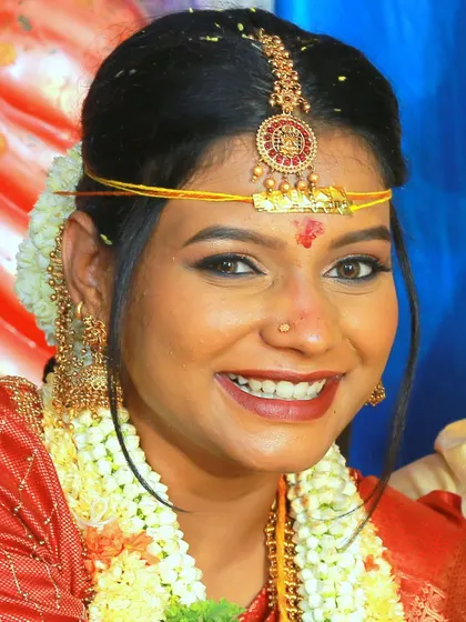 A close-up, happy portrait of a bride in a red saree, adorned with flowers.