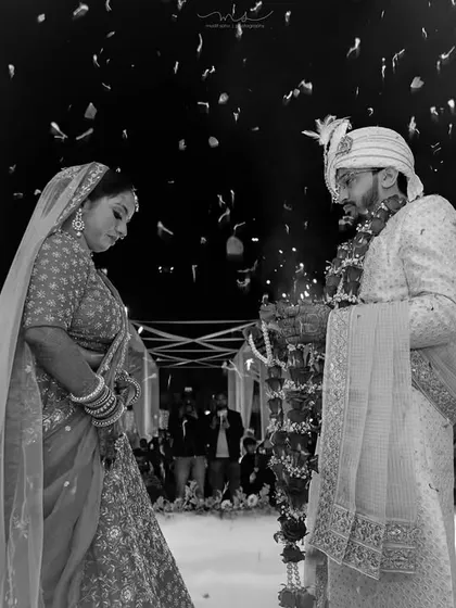 We capture the dramatic and emotional peak moments of your wedding day. This black and white photograph shows the bride and groom during the Varmala ceremony, framed by fireworks and smoke for a truly cinematic feel.