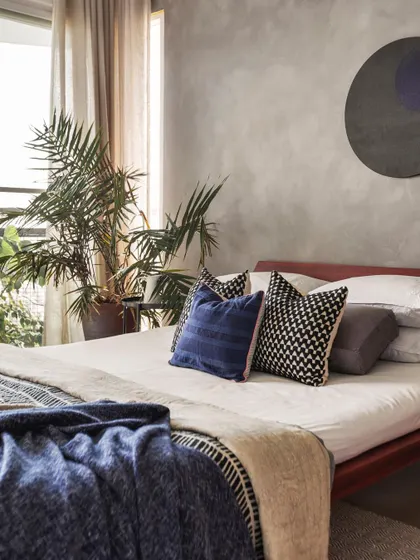 A closer look at the bedding and plant details in the 'Rustic Minimal' bedroom. The textures of the throw blanket and the natural form of the plant add layers of comfort and life to the room.
