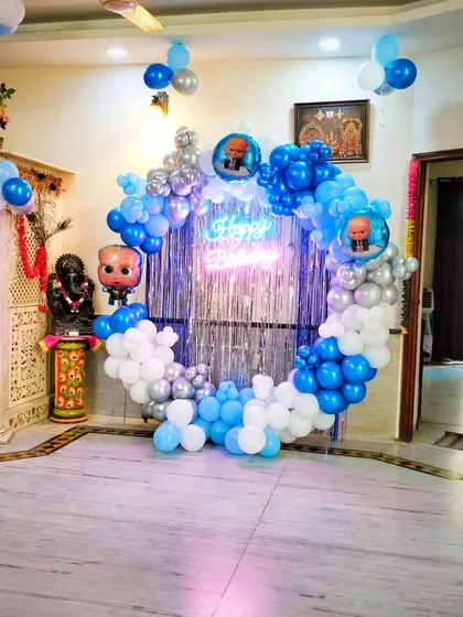 A Boss Baby themed balloon ring backdrop set up in a home. The blue, white, and silver balloons, along with the shimmering curtain, create a fantastic photo corner.