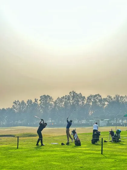 Two golfers in perfect sync with their follow-throughs against a hazy, atmospheric sky.