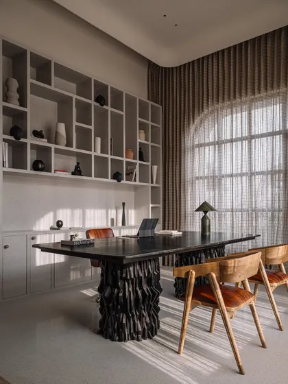 The main study area in the home office, featuring a massive desk with a sculptural base and a backdrop of a full-height shelving unit. The large arched window floods the space with natural light.