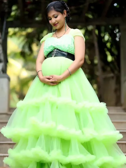 A serene shot of a woman in a lime green maternity gown, looking down at her baby bump.
