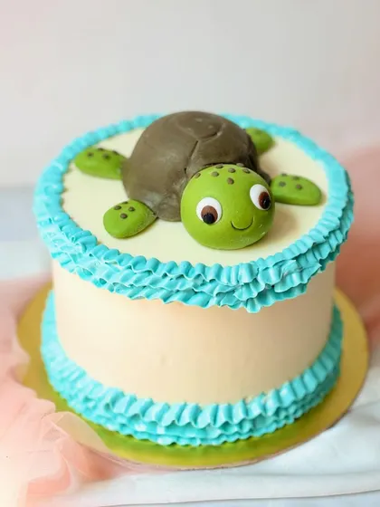 A simple and sweet turtle cake. The friendly turtle is sculpted from fondant and sits on a buttercream cake with a blue ruffled border.
