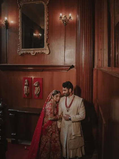 A classic, elegant portrait of the couple in their wedding attire, set against a rich, wood-paneled interior.