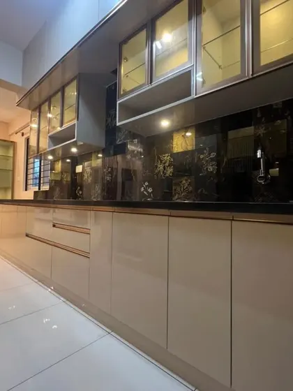A luxurious parallel kitchen with high-gloss beige cabinets, glass-fronted upper units, and a stunning black marble-patterned backsplash. The rose gold handles add a final touch of opulence.