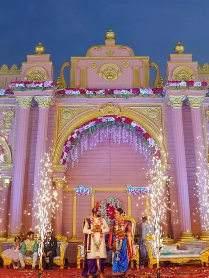 A spectacular wide shot of the wedding stage, with the couple framed by a grand pink palace-like structure and sparkling fireworks.