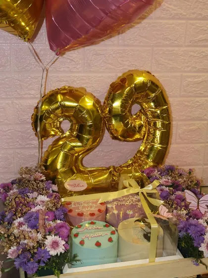 A beautiful birthday gift setup featuring two of our mini cakes nestled in a crate of flowers with a big "29" balloon. A perfect way to celebrate a milestone.