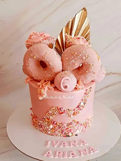 A stunning zero-fondant cake for twin sisters. This all-pink creation is decorated with shimmering sprinkles, edible donuts, and a golden palm spear for a fun and glamorous look.