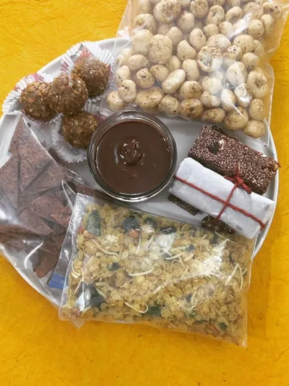 A well-lit shot of my travel snack platter. It shows a variety of healthy options like energy balls, spiced makhana, nutritional bars, and millet mixture, perfect for a journey.
