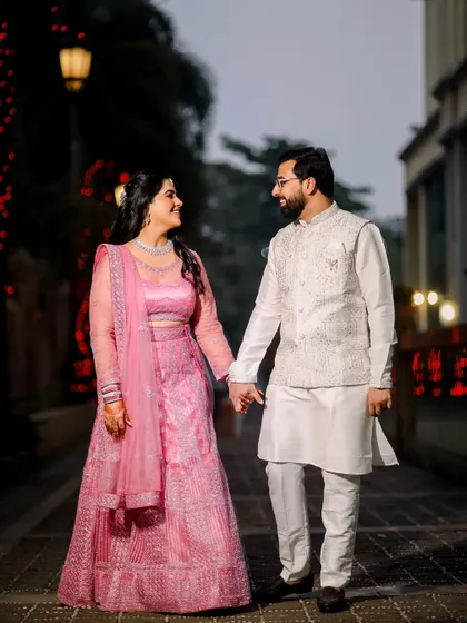 The couple takes a romantic walk, holding hands and sharing a smile. This full-length candid shot captures a happy, relaxed moment from their engagement celebration.