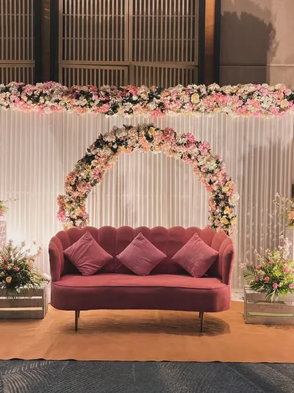 A lovely Roka or engagement stage with a circular floral arch. The arch, made of pink and white flowers, perfectly frames the deep pink sofa, creating a beautiful focal point.