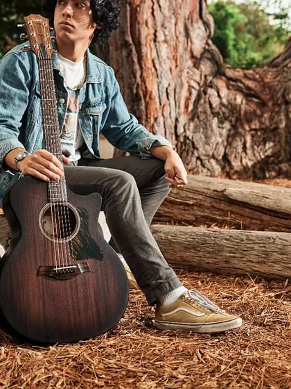 A lifestyle shot featuring the all-new Taylor American Dream AD24ce. This guitar combines solid wood construction with V-Class bracing for a rich tone that's accessible to more players.