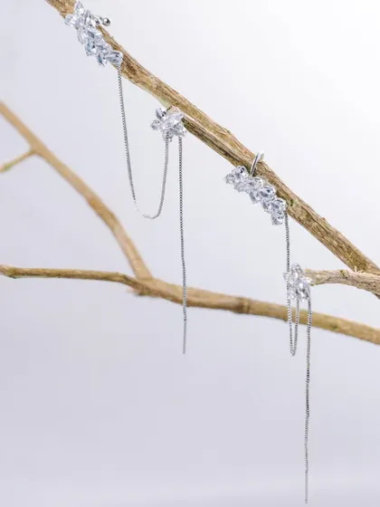 A creative jewellery shot with delicate silver earrings hanging from a natural tree branch, blending elegance with nature.