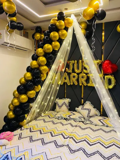 A closer look at the bed area in the black and gold 'Just Married' setup. This shows the details of the balloon garland and the soft lighting from the fairy light canopy, perfect for a newlywed couple.