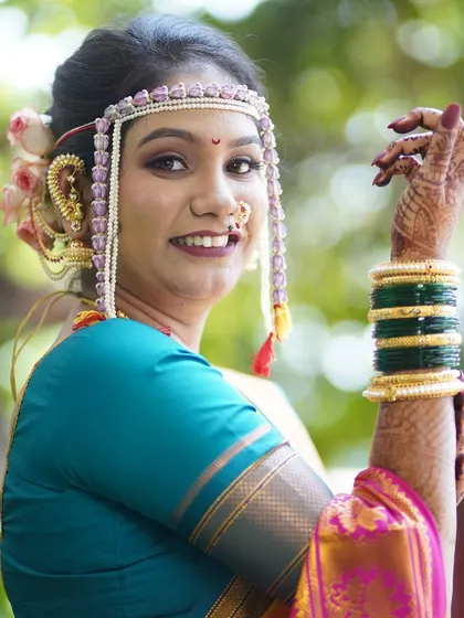 The pure joy of a bride on her special day. This close-up highlights the traditional Maharashtrian bridal accessories, including the 'mundavalya' (forehead ornament), paired with a radiant makeup look that emphasizes her glowing skin and happy smile.