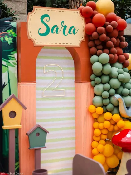 A close-up of the custom 'Sara' sign and the number '2' arch, framed by a vibrant, earthy-toned balloon garland. These details add color and personality to the main stage.