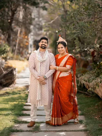 A classic portrait of a Bengali couple in their traditional wedding attire, set in a beautiful garden path.