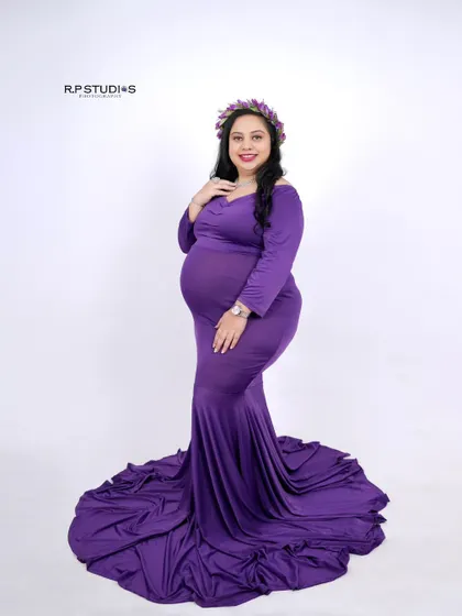 A simple and elegant portrait. The mom-to-be wears a beautiful purple gown and a delicate floral crown, radiating a quiet confidence.