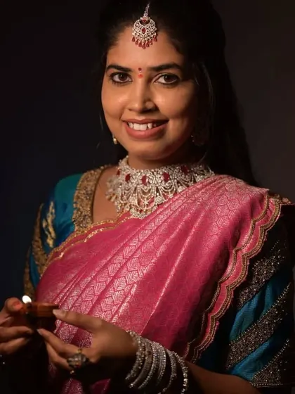 A client holding a diya, dressed in a beautiful pink and blue half saree with an embroidered blouse.