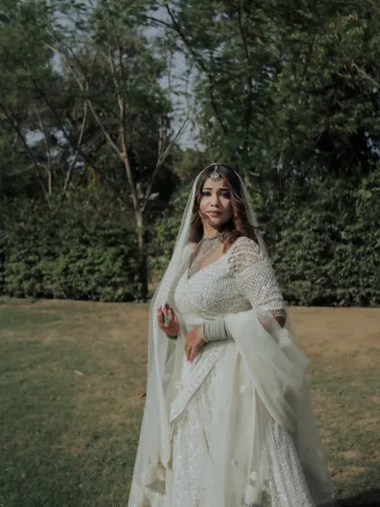 A beautiful outdoor portrait of the bride Shifna, her white lehenga standing out against the lush green background.