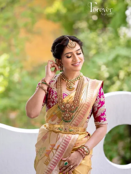 This bride looks absolutely radiant in her pink and gold ensemble. The custom blouse features detailed embroidery that perfectly matches her Kanchivaram saree.